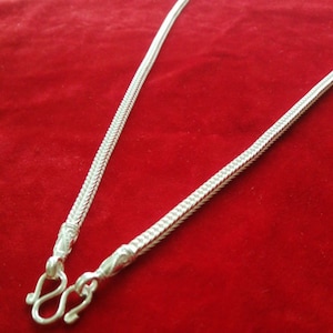 May include: A silver chain necklace with a unique, intricate design. The chain is flat and has a textured surface. The necklace has a hook clasp.