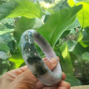 May include: A smooth, polished bangle bracelet featuring a marbled appearance with swirling patterns of translucent white, soft lavender, and deep forest green tones throughout the circular stone band, showcasing a glossy and reflective surface finish.