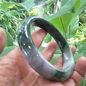 以下が含まれることがあります： 深いフォレストグリーンと柔らかなラベンダーの色合いが混ざり合った、天然石製の滑らかで磨き上げられたバングルブレスレット。円形のアクセサリーは丸みを帯びた形状で、全体に光沢のある反射面を備えています。