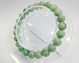 May include: A bracelet made of round, light green jade beads. The bracelet is presented on a clear, circular display stand. The jade beads have a marbled effect with different shades of green.