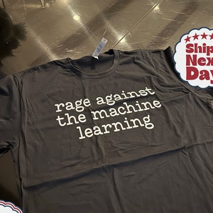 May include: Black t-shirt with white text that reads "rage against the machine learning".