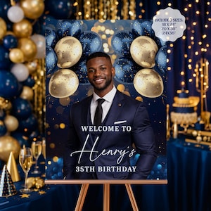 以下が含まれることがあります： ネイビーブルーの誕生日のパーティーサイン。笑顔の男性の写真、金とネイビーの風船、そして「WELCOME TO Henry's 35TH BIRTHDAY」というテキストが特徴です。サインは木製のイーゼルに表示されています。3つのサイズが含まれています：45.7 x 61cm、50.8 x 76.2cm、61 x 91.4cm。