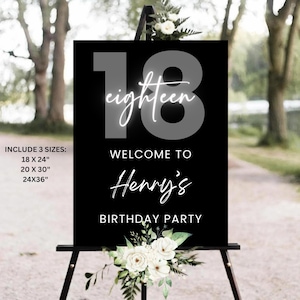 May include: Black sign with the number "18" and the word "eighteen" in a cursive font. The sign reads "Welcome to Henry's Birthday Party." White floral arrangements are at the top and bottom. The sign is displayed on a black easel.