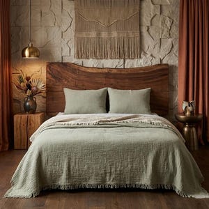 May include: A bedroom scene with a wooden headboard, sage green bedding, and matching pillows. A beige throw blanket adds texture. The room is decorated with a woven wall hanging, dried flowers, and rust-coloured curtains.