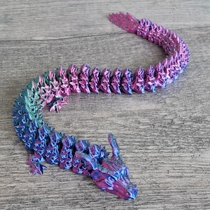 May include: A 3D printed dragon figurine with a segmented body, iridescent blue and pink paint, and a detailed head with horns.