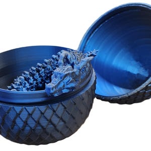 May include: A blue dragon egg-shaped trinket box with a dragon head sculpture inside. The box is made of plastic and has a textured surface.
