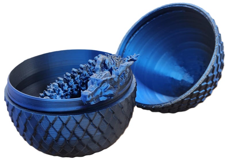 May include: A blue dragon egg-shaped trinket box with a dragon head sculpture inside. The box is made of plastic and has a textured surface.
