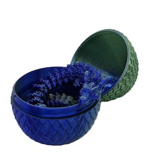 May include: A blue and green dragon egg-shaped container with a dragon figurine inside. The container is made of plastic and has a textured surface.