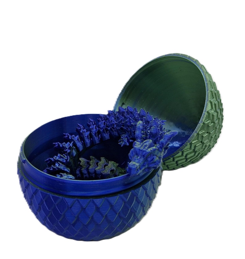 May include: A blue and green dragon egg-shaped container with a dragon figurine inside. The container is made of plastic and has a textured surface.