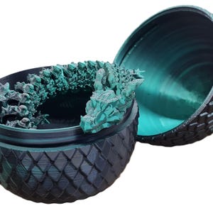May include: A teal green dragon figurine inside a black and teal green dragon egg-shaped container. The container is made of plastic and has a textured surface.