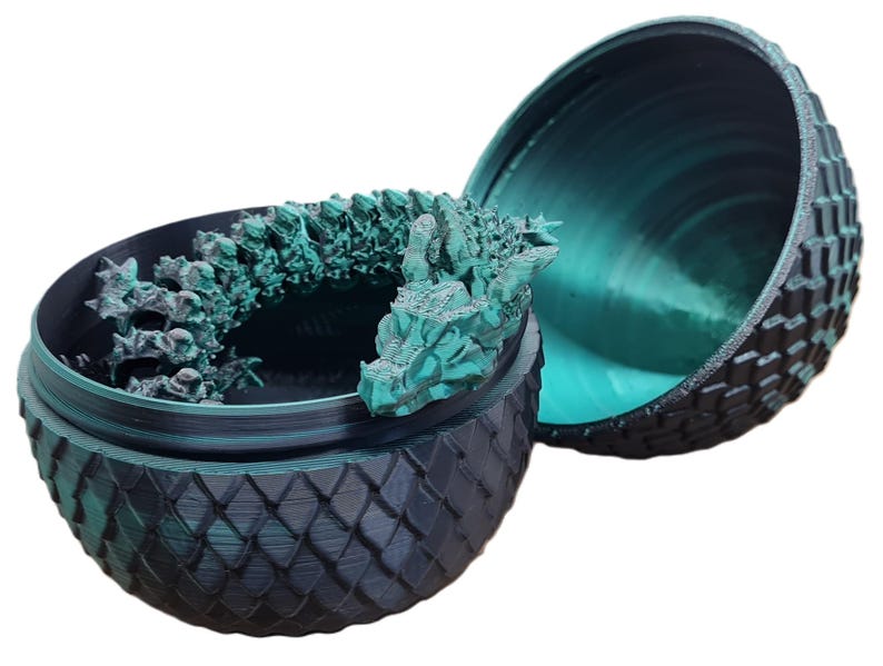 May include: A teal green dragon figurine inside a black and teal green dragon egg-shaped container. The container is made of plastic and has a textured surface.