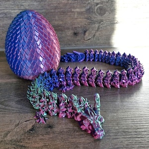 May include: A purple and blue dragon egg with a matching dragon tail made of scales. The egg and tail are made of a shiny, iridescent material.