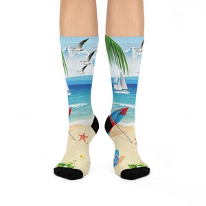 May include: A pair of colorful socks with a beach scene design. The socks feature a sailboat, palm trees, seagulls, and a beach umbrella. The socks are white with blue, green, red, and yellow accents.