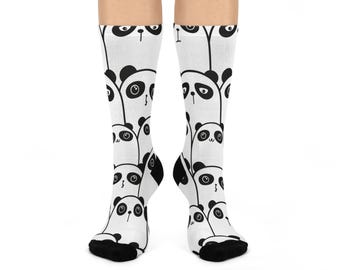 Op de afbeelding: Witte sokken met een herhaald patroon van zwart-witte panda gezichten. De sokken hebben zwarte hielen en tenen. De panda's hebben zwarte oren en ogen.