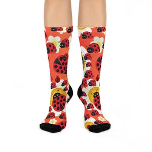 May include: A pair of colourful socks with a pattern of ladybirds on an orange background. The socks are black at the toes and heels.