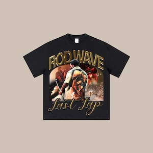 May include: Black t-shirt with a graphic print of a man in a crowd. The text "Rod Wave" and "Last Days" is printed in gold on the shirt.