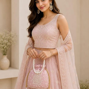 Puede incluir: Conjunto formal bordado en rosa claro, que incluye top, falda y bufanda transparente. El conjunto se complementa con un bolso con cordón rosa a juego con detalles de perlas y asas doradas. Adecuado para ocasiones especiales.
