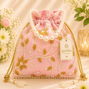 May include: A light pink drawstring pouch bag featuring gold thread floral embroidery, white pearl bead accents, and a pearl bead handle. A white rectangular tag attached to the bag displays the text guniba HANDLOOM with a floral icon and a heart.