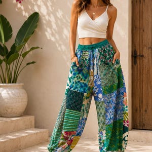 May include: A white ribbed sleeveless crop top with a V-neckline paired with loose-fitting, high-waisted trousers featuring a vibrant patchwork design in shades of green, blue, and yellow with various floral and geometric patterns and side pockets.