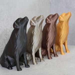May include: Five geometric dog sculptures in a row, in shades of black, beige, brown, and gold. The dogs are sitting with their heads tilted upwards. The sculptures are displayed on a white surface against a grey wall.