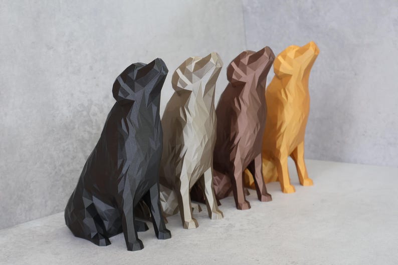 May include: Five geometric dog sculptures in a row, in shades of black, beige, brown, and gold. The dogs are sitting with their heads tilted upwards. The sculptures are displayed on a white surface against a grey wall.