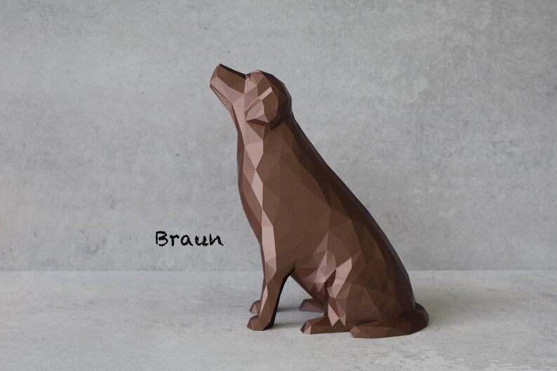 May include: A brown geometric dog sculpture in a sitting position, with its head tilted upwards. The word "Braun" is written in black script on the lower left. The sculpture is on a light gray surface against a matching background.