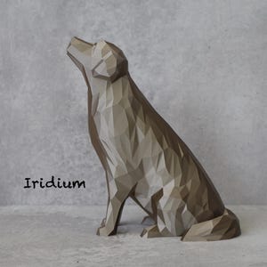 May include: A geometric dog sculpture in shades of grey and brown, with a textured, faceted design. The dog is sitting and looking upwards. The word "Iridium" is printed in black on the lower left.
