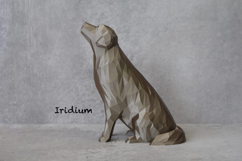 May include: A geometric dog sculpture in shades of grey and brown, with a textured, faceted design. The dog is sitting and looking upwards. The word "Iridium" is printed in black on the lower left.