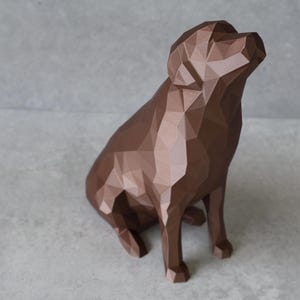 May include: A brown geometric dog sculpture in a sitting position, with its head tilted upwards. The sculpture has a faceted design, creating a modern, angular aesthetic. The dog statue is a decorative item.