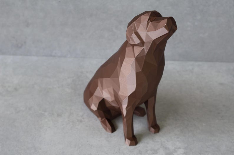 May include: A brown geometric dog sculpture in a sitting position, with its head tilted upwards. The sculpture has a faceted design, creating a modern, angular aesthetic. The dog statue is a decorative item.
