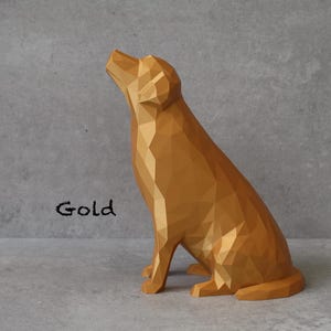 May include: A gold-colored, geometric dog sculpture in a sitting position, with its head tilted upwards. The word "Gold" is written in black script below the dog. The sculpture has a faceted design.