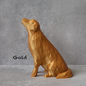 May include: A gold-coloured, geometric dog sculpture in a seated position, with its head tilted upwards. The word "Gold" is written in black script on the left side of the sculpture. The dog has a faceted design, giving it a modern look.