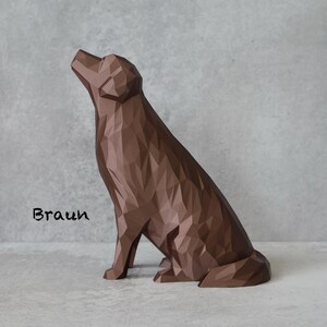 May include: A brown geometric dog sculpture in a seated position, with its head tilted upwards. The sculpture has a faceted design and is set against a grey background. The word "Braun" is written in black cursive.
