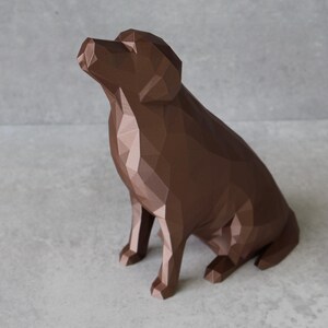 May include: A brown geometric dog sculpture in a sitting position, with its head tilted upwards. The sculpture has a low-poly design, with many flat surfaces creating its form. The dog is a solid, rich brown color, and the background is a light gray.