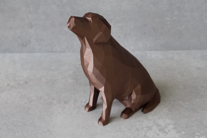 May include: A brown geometric dog sculpture in a sitting position, with its head tilted upwards. The sculpture has a low-poly design, with many flat surfaces creating its form. The dog is a solid, rich brown color, and the background is a light gray.