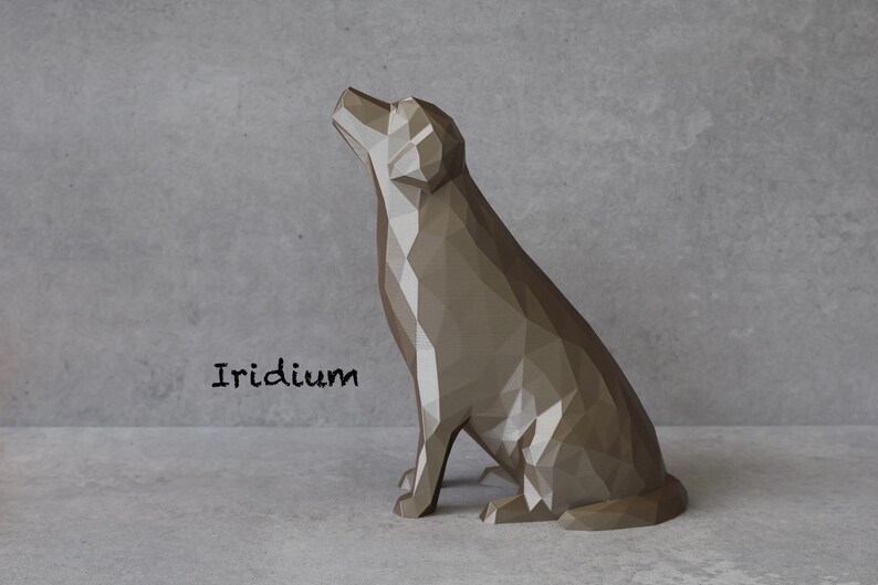 May include: A geometric, polygonal dog sculpture in a seated position, with its head tilted upwards. The sculpture is a muted, metallic brown color and is set against a gray backdrop. The word "Iridium" is printed in black.