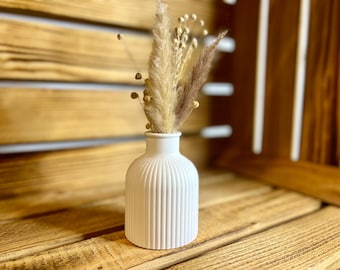 May include: A white ceramic vase with vertical ridges, holding a bouquet of dried pampas grass and other dried flowers.