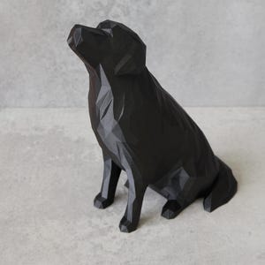 May include: A black geometric dog sculpture. The dog is sitting with its head tilted upwards. The sculpture has a faceted design, giving it a modern and artistic look. The dog is made of a solid black material.