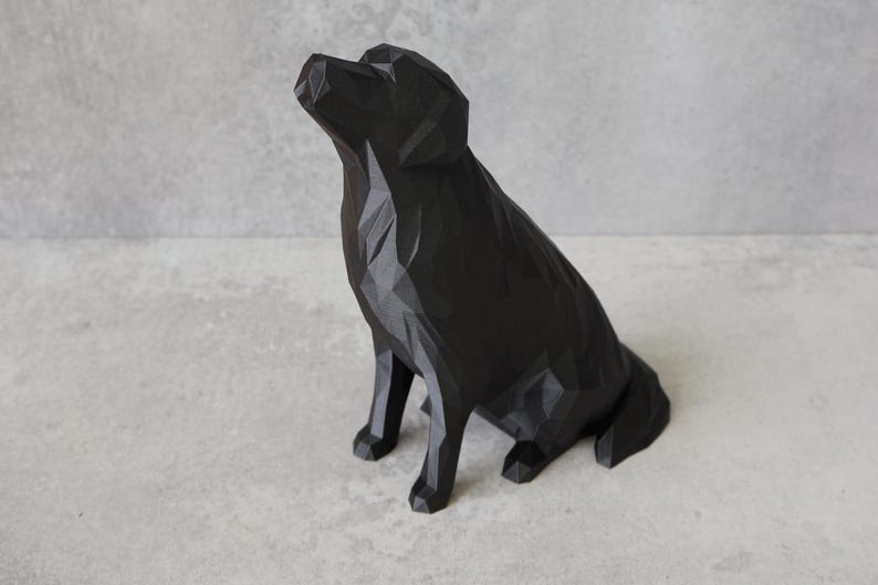 May include: A black geometric dog sculpture. The dog is sitting with its head tilted upwards. The sculpture has a faceted design, giving it a modern and artistic look. The dog is made of a solid black material.