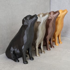 May include: A row of five geometric dog sculptures in shades of black, gray, beige, brown, and gold. The dogs are in a sitting position with their heads tilted upwards. The sculptures are displayed on a light gray surface.
