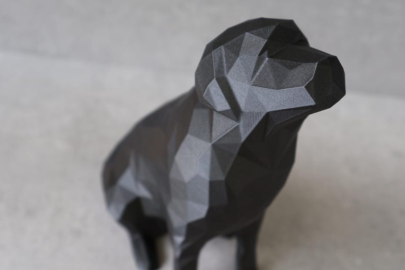 May include: A black geometric dog sculpture. The dog is depicted in a low-poly style, with many flat, angled surfaces creating its form. The sculpture is made of a matte black material and stands on four legs, with its head raised.