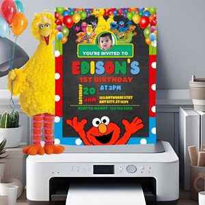 May include: A Sesame Street themed birthday invitation with a photo of a child in the center. The invitation is printed on a white printer with a yellow Big Bird plush toy holding balloons in the background. The text on the invitation reads "You're invited to Edison's 1st Birthday, Saturday, Jan 20 at 3pm, 123 Anywhere St, Any City, St 1234, RSVP to Mommy: 123 456 7890".