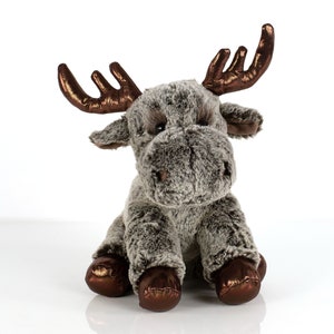 Peut inclure: Un jouet en peluche de couleur gris en forme d'élan avec des bois marrons. L'élan est assis avec ses pattes repliées sous son corps. Le jouet a une texture douce et pelucheuse.
