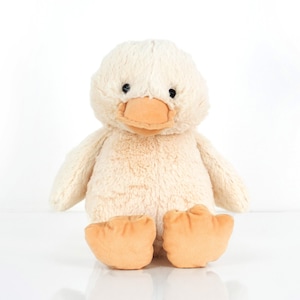 Puede incluir: Un juguete de peluche de pato de color crema con un pico marrón y ojos negros. El pato está sentado sobre una superficie blanca.