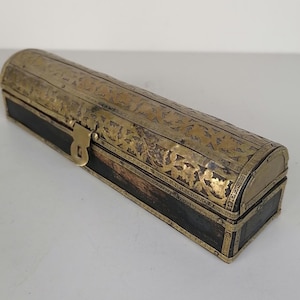 May include: A rectangular, antique-style box with a curved lid. The box is made of dark wood and is accented with brass metal. The brass features intricate floral patterns and a small latch. The box is approximately 10 inches long.