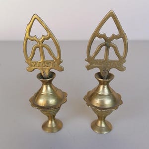 Può includere: Due antichi applicatori per eyeliner al kohl in ottone. Ogni applicatore ha una parte superiore traforata decorativa con la scritta "MADE IN" e un corpo bulboso. Gli applicatori sono su una superficie bianca.