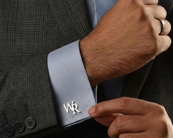 May include: Silver cufflinks with the initials "WR" on a light blue dress shirt. The shirt is paired with a gray plaid suit jacket. The image shows a close-up of the cufflink and the suit.