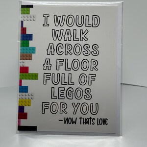 May include: A white greeting card with the text "I WOULD WALK ACROSS A FLOOR FULL OF LEGOS FOR YOU - NOW THATS LOVE" in black. The left side features colorful Lego bricks.