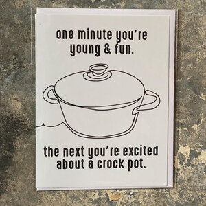 Puede incluir: Una tarjeta blanca con texto negro que dice "one minute you're young & fun. the next you're excited about a crock pot." Un dibujo en blanco y negro de una olla de cocción lenta está en el centro de la tarjeta.