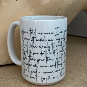 May include: White ceramic coffee mug with black handwritten text that reads "Mama told me when I was young, Come sit beside me, my only son, And listen closely to what I say, And if you do this it'll help you on your way. Take your time, don't be in a hurry, Troubles will come and they will try you. You'll find a woman and you will love her. And don't forget, son. There is a time for everything."